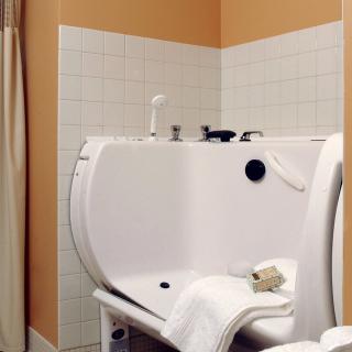 An accessible bathtub featuring a side door, set in a tiled bathroom with towels and a showerhead.
