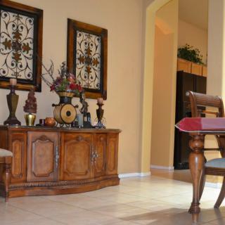 A cozy living room interior featuring a wooden cabinet adorned with vases and artwork, alongside a partially visible dining table.