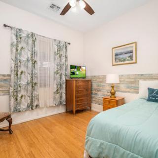 A cozy and well-decorated bedroom featuring wood flooring, a comfortable bed with light blue bedding, and decorative curtains.