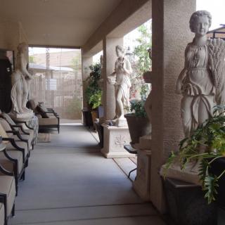 A corridor adorned with classical sculptures and indoor plants, featuring comfortable seating.