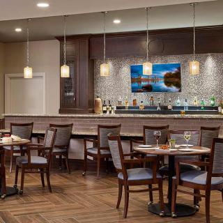 A modern restaurant interior with a bar, featuring tables and chairs, pendant lighting, and wood flooring.