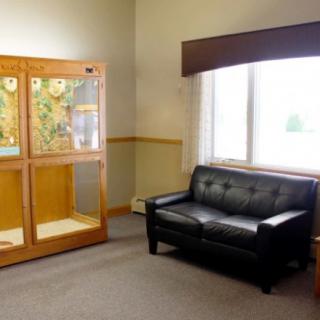 A small lobby featuring a black couch and a wooden display case near a window.