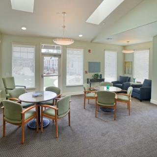 A cozy living area with tables, chairs, and sofas, featuring large windows.