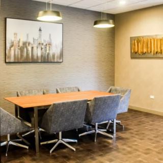 A modern conference room featuring a wooden meeting table surrounded by office chairs, adorned with contemporary artwork on the walls.