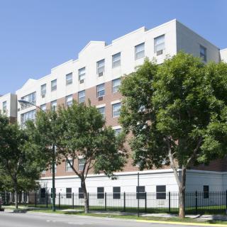 A multi-story residential building with trees lining the street in an urban setting.