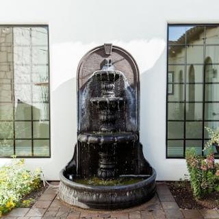 A beautiful outdoor fountain surrounded by greenery, framed by large windows.