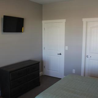 A bedroom with a wall-mounted TV, dresser, and two doors in neutral tones.