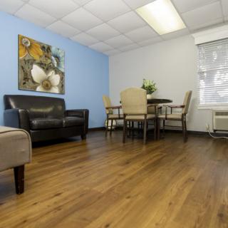 A cozy waiting room with a sofa, table, and chairs, adorned with artwork on the wall.