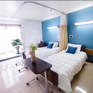 A clean and bright hospital room with two beds, featuring blue accent walls and modern furnishings.