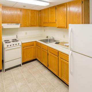 A clean and simple kitchen with wooden cabinets, a refrigerator, stove, and sink.