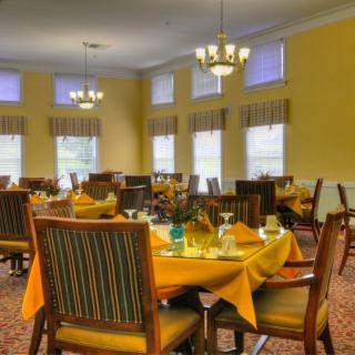 A well-lit dining room with neatly set tables and elegant chandeliers.