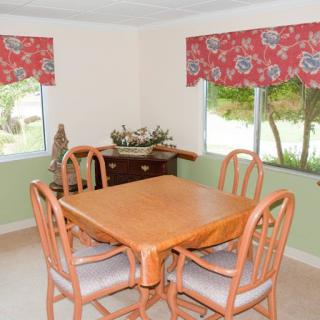 A cozy dining nook featuring a wooden table surrounded by chairs, with floral window treatments allowing natural light to brighten the space.