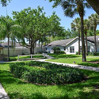 A picturesque residential area featuring lush green lawns, trees, and a pathway leading to charming houses.