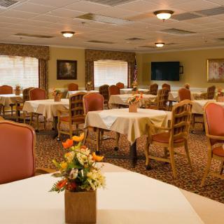 A warmly decorated dining room with tables and chairs, featuring floral centerpieces.