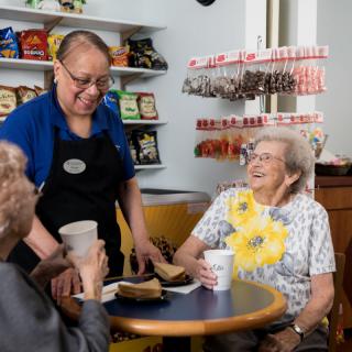 A friendly interaction in a cafe between staff and elderly patrons.