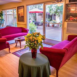 A cozy living room with red sofas and a vase of flowers, illuminated by natural light through glass doors.