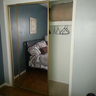 A bedroom with mirrored closet doors revealing an interior containing blankets and hangers.