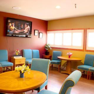 A cozy waiting room with blue chairs, tables, and a wall-mounted television.
