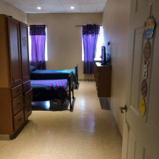 A cozy bedroom with two beds and purple curtains, viewed from the doorway.
