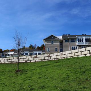 A large residential house with a stone wall and green lawn under a clear blue sky.
