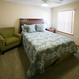 A cozy bedroom featuring a bed with floral bedding, an armchair, and a bedside table with a lamp.
