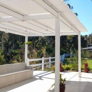 A sunny outdoor patio with a white pergola and garden view.