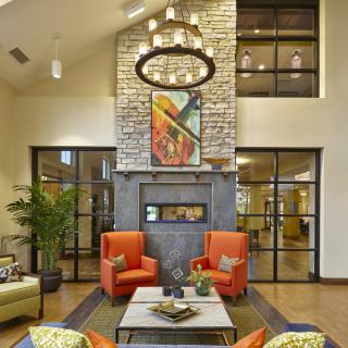 A modern living room with a striking fireplace and bold orange chairs, complemented by contemporary art and a stylish chandelier.