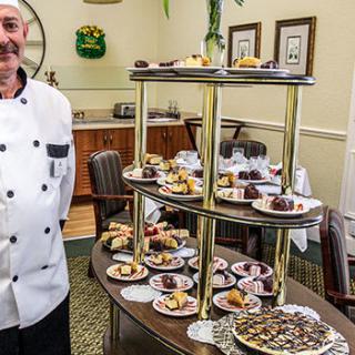 A chef standing beside a buffet table filled with an assortment of desserts and pastries.