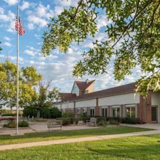 A beautiful view of a building surrounded by lush greenery and under a partly cloudy sky, featuring an American flag.
