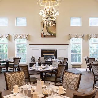 An elegant dining room setup with multiple tables, a chandelier, and a fireplace.
