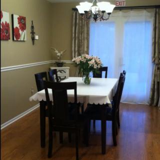 A cozy dining room with a table set for four, featuring a chandelier and flower centerpiece.