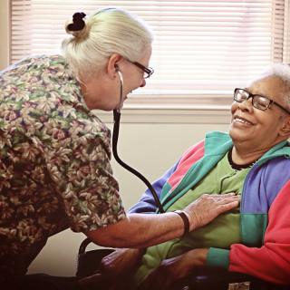 A healthcare professional conducts a medical examination on a smiling patient using a stethoscope.