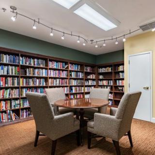 A cozy library with bookshelves and a round table surrounded by chairs.