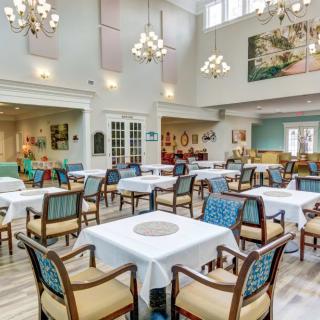 A spacious and well-lit dining room with neatly arranged tables and chairs, adorned with elegant chandeliers.