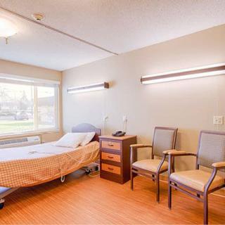 An empty hospital room with a bed, two chairs, and a window, creating a clean and quiet atmosphere.