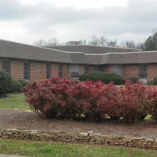 A view of a modest building surrounded by colorful bushes under a cloudy sky.