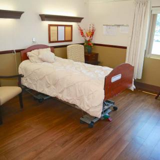 A clean and minimalistic hospital room with a single bed and wooden flooring.