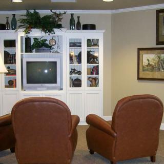 Cozy living room setup with leather chairs facing a television and decorative shelving.