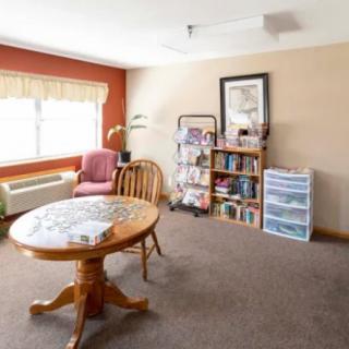 A cozy room featuring a round table, bookshelf, and a comfortable chair by the window.