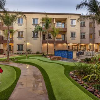 A residential apartment complex with a landscaped garden and pathway, surrounded by palm trees.