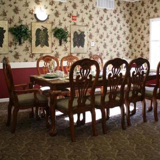 A traditional dining room with a long wooden table and matching chairs, adorned with classic floral wallpaper and wall art.