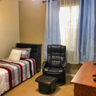 A cozy bedroom with a single bed, black reclining chair, and wooden desk.