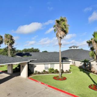 A residential home with a well-maintained lawn and palm trees under a clear blue sky.
