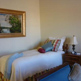 A cozy bedroom with a single bed, colorful pillows, and a painting on the wall.