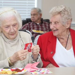 Two elderly women enjoy a friendly conversation while engaging in an arts and crafts activity.