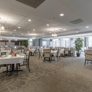 A spacious dining area with elegantly set tables and chairs, complemented by chandeliers and stylish decor.