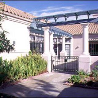 A sunny courtyard with a gated entrance, surrounded by lush garden plants and featuring classic architectural elements.