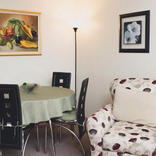 A cozy dining nook with a round table, surrounded by chairs and a floor lamp, adjacent to a patterned sofa. The walls are adorned with colorful artwork.