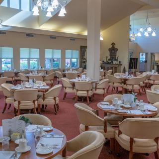 An elegant dining room with neatly arranged tables and chairs, featuring chandeliers and a red carpet.