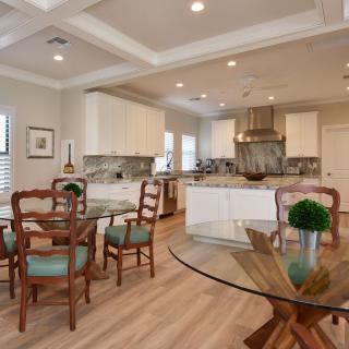 A modern open-concept kitchen and dining area with wood flooring, glass tables, and white cabinets.